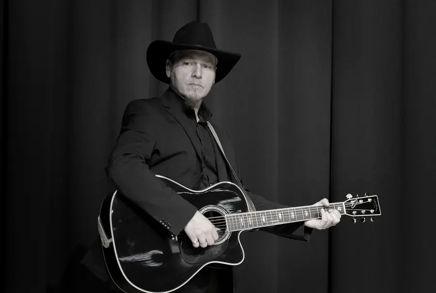Roman Hofbauer mit Hut und Akustikgitarre im Querformat, Foto M. Kriegl